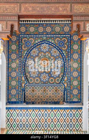 Una nicchia fontana murale decorativa a Dar Jamai ha un arco a ferro di cavallo che incornicia una superficie a mosaico zellige con motivi geometrici blu e verdi sopra un piccolo Foto Stock