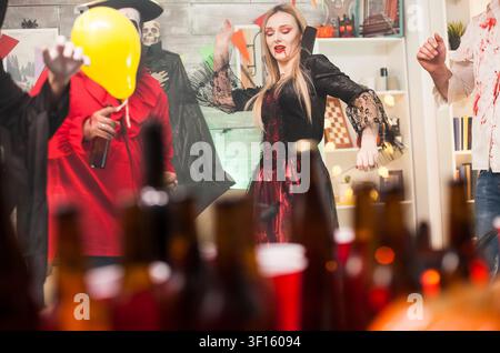 Bella giovane donna vestita da vampiro mostra movimenti di danza a una festa di Halloween con amici, combinando costumi da mostro e interazione sociale. Foto Stock