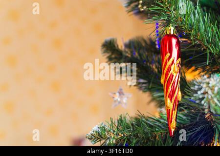 Decorazione natalizia a forma di ghiacciolo rosso appesa a un ramo di abete con spazio libero. Decorazione per le feste e concetto di celebrazione festiva per auguri stagionali Foto Stock