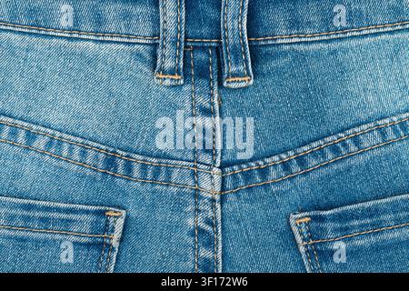Macro dettagliata di tessuto denim blu. Il primo piano mostra la texture classica, le cuciture gialle, gli occhielli per la cintura, la cucitura della tasca posteriore Foto Stock