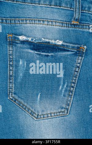 Macro dettagliata della tasca posteriore di jeans blu in denim. Tessuto consumato e sfilacciato e cuciture arancioni creano uno stile vintage e casual. Fondo testurizzato perfetto Foto Stock