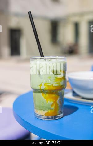 Close-up di un latte freddo al matcha e mango con cubetti di ghiaccio in un bicchiere alto su un tavolo Foto Stock