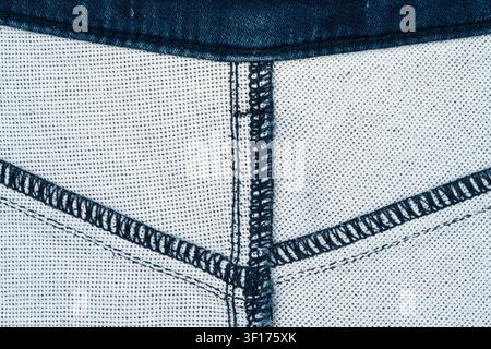 Vista macro di tessuto denim che mostra intricati motivi di cucitura e una trama tessuta. Toni blu e bianchi con forte contrasto. Ideale per moda, tessile, d Foto Stock