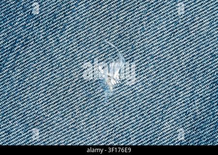 Macro dettagliato del tessuto di jeans blu. Trama diagonale a twill con un piccolo buco strappato e fili bianchi sfilacciati. Concetto di abbigliamento usato per la moda Foto Stock