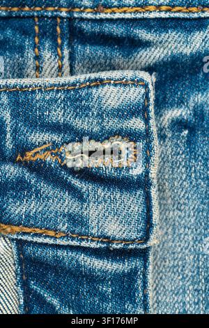 Estremo primo piano di tessuto di jeans blu consumato. La ripresa macro mostra la trama dettagliata, l’asola e le cuciture a contrasto. Concetto classico di abbigliamento casual per Foto Stock