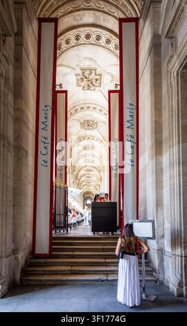 Una donna in abito estivo dà un'occhiata al menu all'ingresso del Cafe Marly a Parigi, in Francia, un famoso ristorante situato nel palazzo del Louvre. Foto Stock