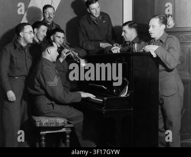I soldati dell'esercito britannico si rilassano durante la Seconda Guerra Mondiale radunandosi intorno a un pianoforte verticale per un canto informale. Un soldato suona il pianoforte mentre un altro accompagna alla tromba e i compagni soldati cantano, illustrando la cameratismo in tempo di guerra e l'intrattenimento fuori servizio negli anni '40. Foto Stock