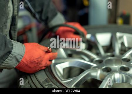 Una persona lavora per riparare una gomma in un'officina. Indossa guanti e si concentra per assicurarsi che la gomma sia pronta per l'uso. Gli attrezzi sono vicini sul banco da lavoro. Foto Stock