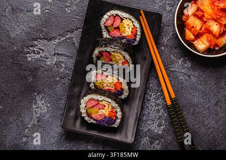 Un piatto nero pieno di kimbap (o gimbap) con ripieni colorati. Gli ingredienti includono salsiccia, cetrioli, uovo e verdure. Foto Stock