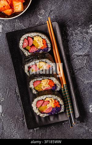 Un piatto nero pieno di kimbap (o gimbap) con ripieni colorati. Gli ingredienti includono salsiccia, cetrioli, uovo e verdure. Foto Stock
