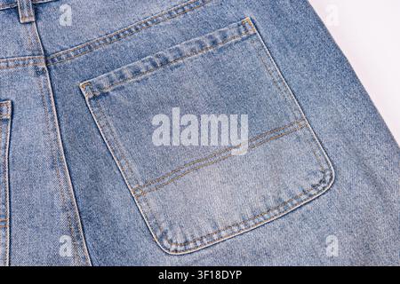 Prima pianura della tasca posteriore di un paio di jeans in denim, cuciture dorate su denim blu chiaro, che enfatizzano la trama e l'artigianalità, sfondo minimalista, illuminazione uniforme Foto Stock