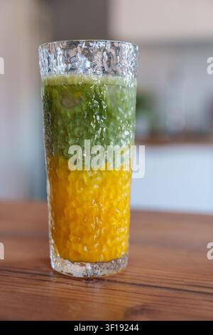 Latte matcha al mango ghiacciato a strati in un bicchiere alto sul tavolo della cucina Foto Stock