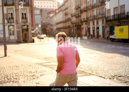 Porto, 11 luglio 2026; Uomo in polo rosa che cammina su una strada acciottolata durante l'ora dorata a Porto. Foto Stock