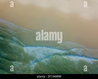 Vista aerea di onde oceaniche turchesi che si infrangono dolcemente su una spiaggia sabbiosa Foto Stock