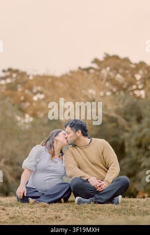 Momento di maternità autunnale pieno d’amore mentre una coppia in attesa condivide un tenero bacio all’aperto, evidenziando affetto, anticipazione e caldi colori stagionali Foto Stock