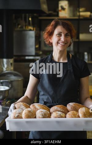 Panettiera sorridente che tiene in mano il pane fresco artigianale in forno Foto Stock