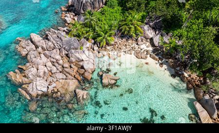Acque cristalline si riversano su grandi rocce di granito, incorniciate da palme verdi lussureggianti e da una spiaggia isolata. Curieuse, Seychelles. Foto Stock