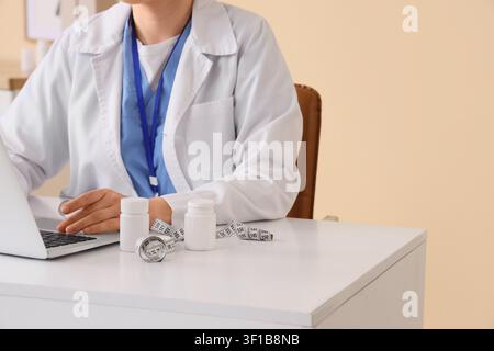 Medico o nutrizionista in camice bianca che lavora su un laptop con metro a nastro e bottiglie di integratori su una scrivania, metro a nastro e bottiglie di integratori Foto Stock