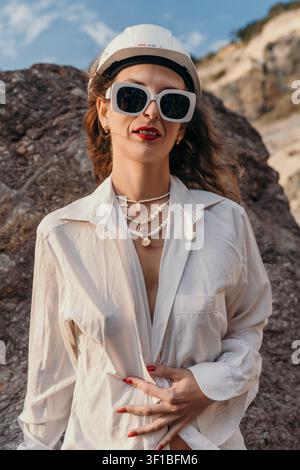 Donna edile Natura Donna alla moda che indossa un casco bianco e occhiali da sole in un paesaggio roccioso durante l'ora dorata Foto Stock