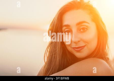 Ritratto di donna al tramonto con una giovane donna felice che sorride all'aperto durante l'ora dorata in spiaggia con un caldo effetto di luce Foto Stock