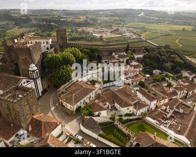 Vista aerea del castello di Obidos con le sue fortificazioni storiche, i tetti in terracotta e le strade strette circondate dalla vegetazione lussureggiante di Obidos, Leiria D Foto Stock