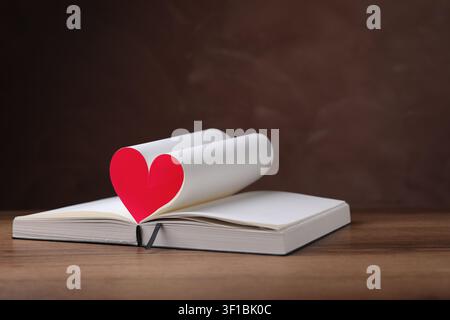 Libro con un cuore fatto di pagine su un tavolo di legno Foto Stock