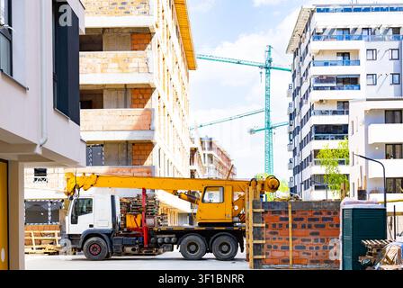 Gru mobile gialla parcheggiata in un cantiere edile urbano di un edificio residenziale con gru torre alte sullo sfondo Foto Stock