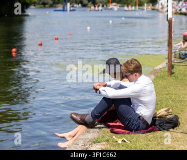 Coppia seduta in riva al fiume, immerge i piedi nell'acqua, godendosi la Henley Regatta Foto Stock