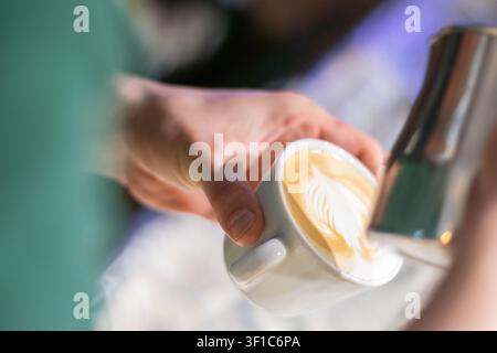 Barista che versa latte vaporizzato nell'espresso creando arte latte Foto Stock