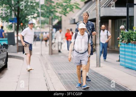 Toronto, Canada - 20 giugno 2026: Uomo anziano che cammina su un marciapiede urbano con pedoni Foto Stock