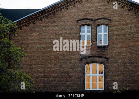 Un vecchio edificio in mattoni con finestre, visto dal basso. Un frammento della facciata storica in mattoni rossi di sera. Luce calda nella finestra. Foto Stock