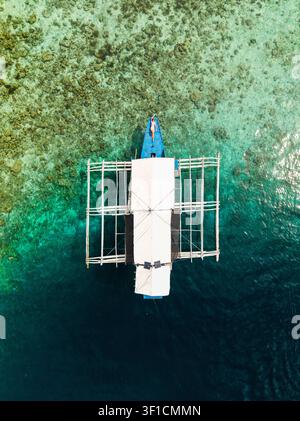 Vista aerea di una donna sdraiata sulla prua di una barca tradizionale con bilanciere che galleggia nelle acque turchesi limpide del mare a Coron, Mimaropa, Filippine Foto Stock