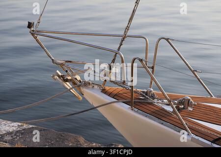 Prima di uno yacht a vela legato a un molo con delle cime, mostra il ponte in teak e le ringhiere in acciaio inossidabile, riflettendo il calmo mare blu in una giornata di sole Foto Stock