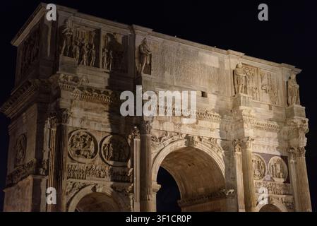 Vista notturna ad angolazione bassa dell'Arco di Costantino illuminato con antiche sculture romane a Roma. Architettura classica monumentale, eredità storica Foto Stock