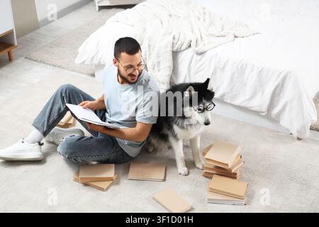 Bel giovane e simpatico cane da husky con gli occhiali che leggono libri sul pavimento a casa Foto Stock