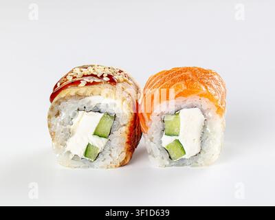 Primo piano di due rotoli di sushi con salmone, cetriolo, crema di formaggio, semi di sesamo e salsa. Fondo bianco pulito e luce soffusa evidenziano le texture e i colori Foto Stock