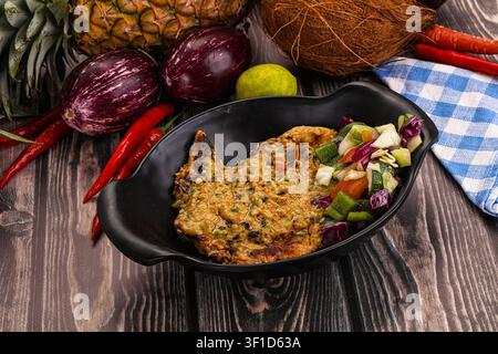 Polpetta di melanzane grigliata servita con cetriolo tritato, cavolo rosso, carota in ciotola nera. Circondata da ananas, noce di cocco, peperoncini, lime su sfondo rustico Foto Stock