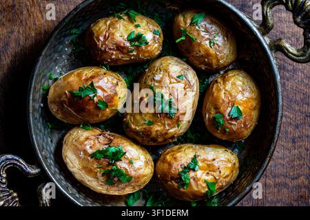 Patate al forno con prezzemolo fresco in padella vintage. Patate intere rustiche cotte al forno con buccia cosparse di sale marino e prezzemolo verde tritato all'interno Foto Stock
