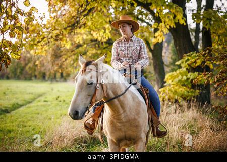 Cowgirl a cavallo nella campagna autunnale. Giovane donna con cappello da cowboy che si gode l'equitazione in stile western Foto Stock