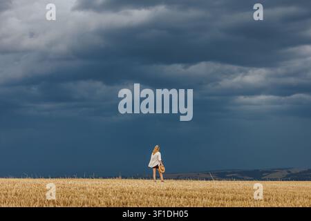Agricoltrice che osserva nuvole tempestose scure sopra un campo agricolo raccolto. Meteo estrema causata dal cambiamento climatico Foto Stock