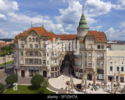 Grande edificio barocco con tetto rosso e torre verde in una piazza affollata sotto un cielo nuvoloso, vista aerea, Palazzo dell'Aquila Nera, Piata Unirii, Unity Square, O Foto Stock