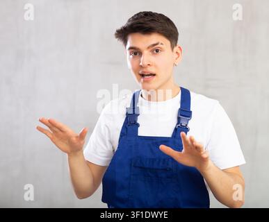 Emozioni, persone e concetto positivo - l'uomo in tute protettive blu esprime diverse su sfondo grigio Foto Stock