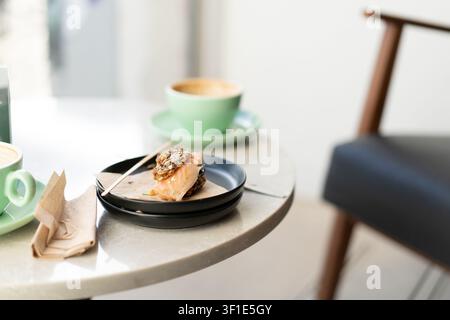 Panino aperto con salmone affumicato servito su un piatto con una tazza di caffè su un tavolo moderno di un caffè. Foto Stock