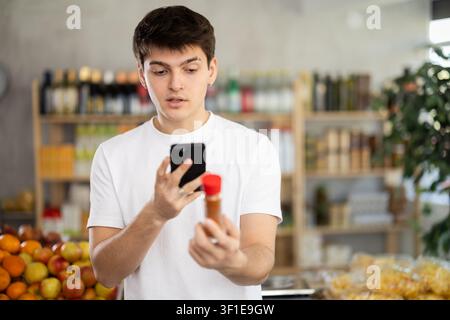 Ragazzo che scansiona il codice QR sull'etichetta del cardamomo in bottiglia nel reparto di alimentari del supermercato Foto Stock