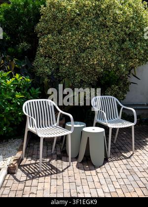 Area di seduta da giardino moderna e vuota con sedie bianche e piante tropicali rigogliose, che crea un'atmosfera accogliente da patio per il relax, vita minimalista Foto Stock
