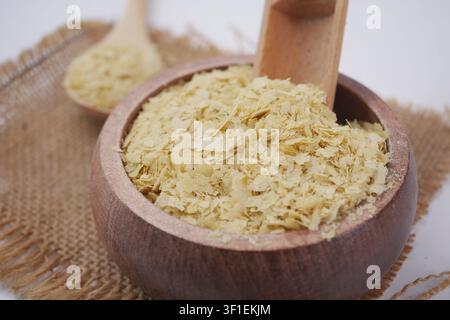 Fiocchi di lievito nutrizionale in una ciotola di legno con cucchiaio su un panno ruvido Foto Stock