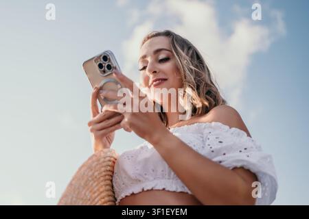 Donna smartphone all'aperto, utente femminile sorridente che tiene un telefono cellulare contro uno sfondo di cielo blu per i social media e la comunicazione Foto Stock