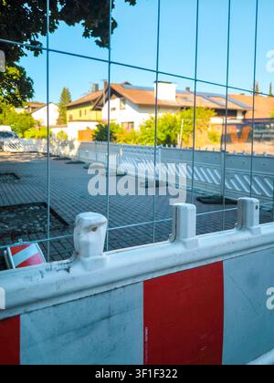 Barriera del cantiere con strisce di avvertimento rosse e bianche in una strada residenziale in Germania, recinzione di sicurezza davanti a un'area di costruzione nuova in una giornata di sole Foto Stock