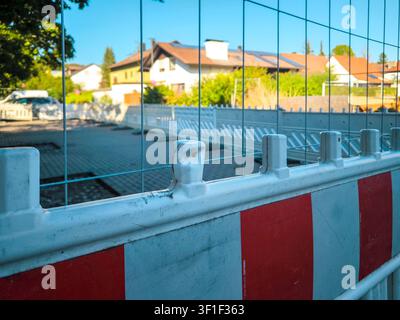 Barriera del cantiere con strisce di avvertimento rosse e bianche in una strada residenziale in Germania, recinzione di sicurezza davanti a un'area di costruzione nuova in una giornata di sole Foto Stock