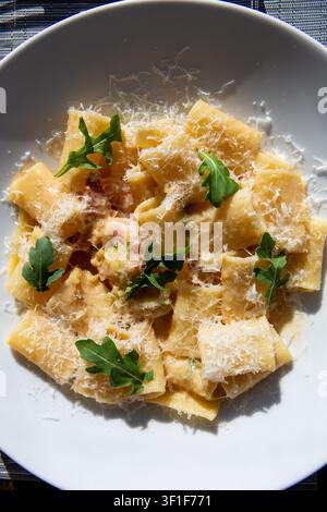 Pasta italiana da ristorante gustosa con una salsa di formaggio cremosa e guarnizione di rucola fresca. Vista dall'alto in piena luce solare. Foto Stock